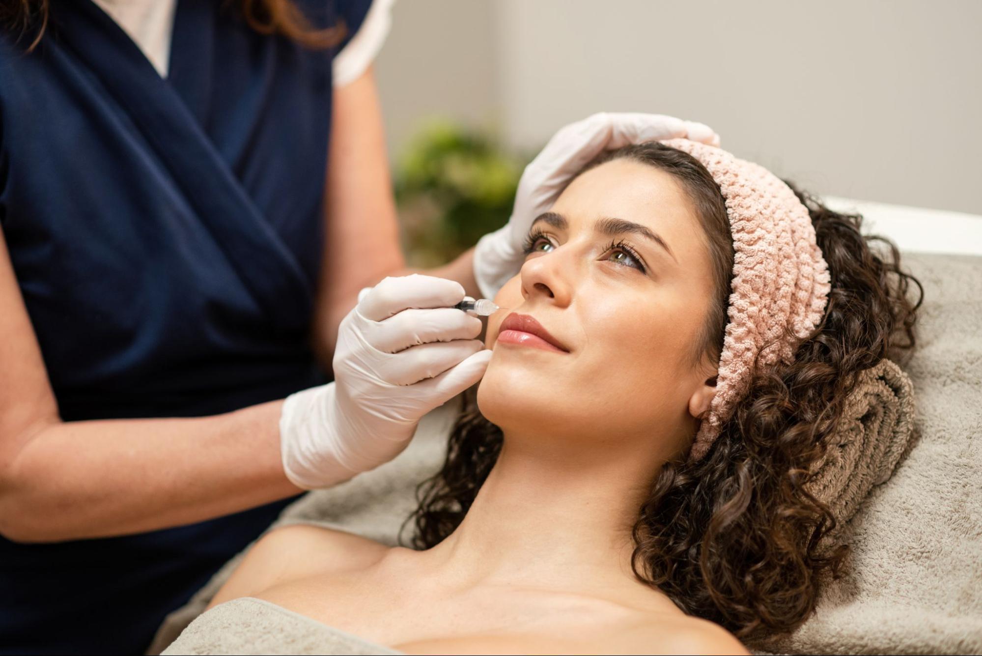 A professional administers a Botox injection to a woman's lips in a clinical setting.