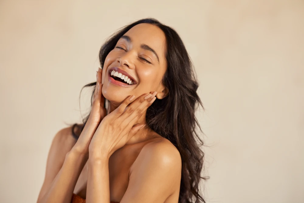 Woman joyfully touching her glowing face after medical spa treatment.